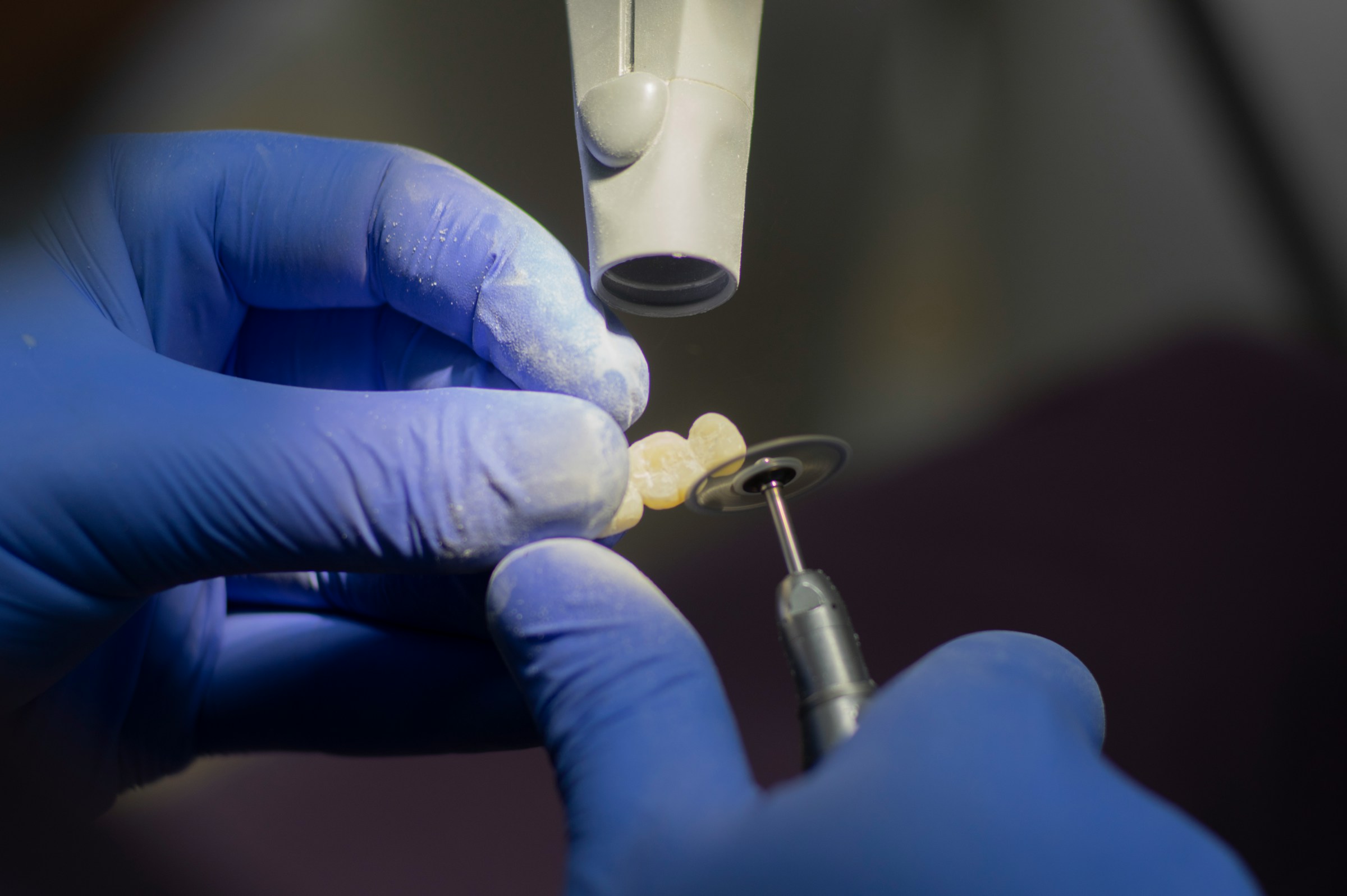 vollkeramikkrone-herstellung-labor-berne Zahntechniker poliert eine Vollkeramikkrone mit einem rotierenden Instrument im Dentallabor